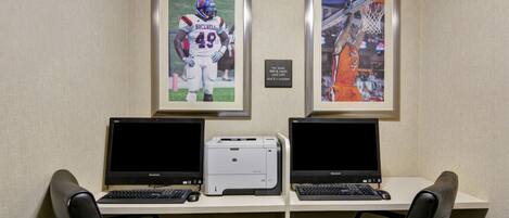A workspace with two desks, each with a laptop and a printer. There are two framed sports photographs on the wall.