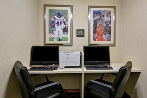 Un espacio de trabajo con dos escritorios, cada uno con una computadora portátil e impresora. Hay dos fotografías enmarcadas de deportes en la pared.