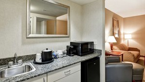 A compact hotel room with a kitchenette, a sink, a microwave, a coffee maker, a small table, a chair, and a bedside lamp. - Hampton Inn Lewisburg (Lewisburg)