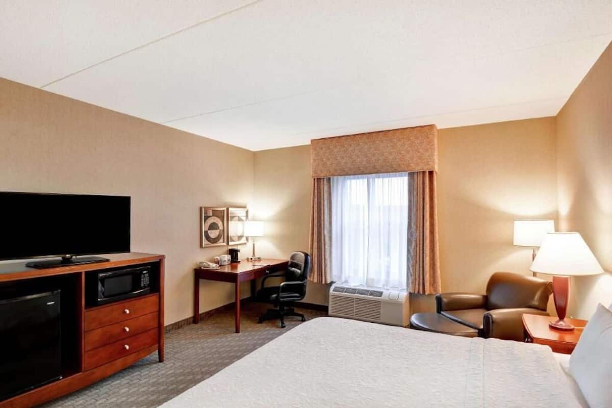 Habitación de hotel con cama, escritorio, silla, televisor y ventana con cortinas.
