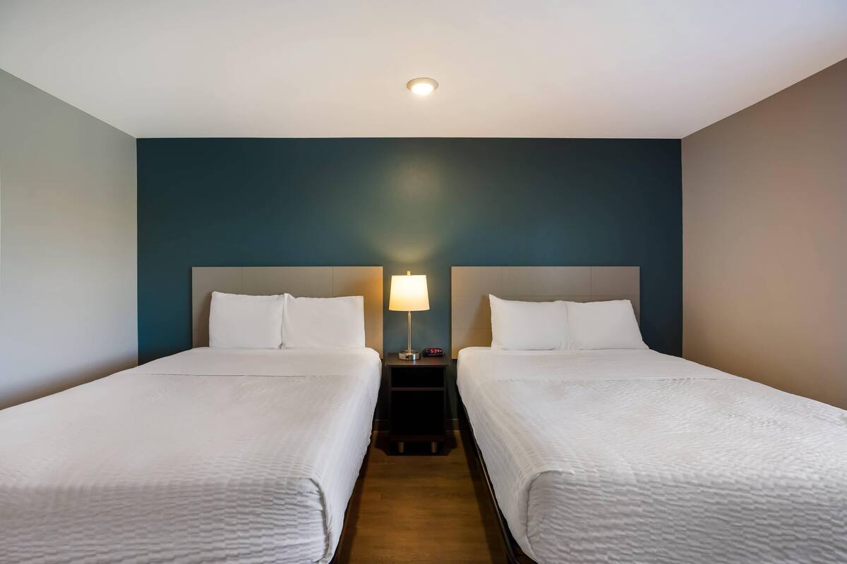 Une chambre d’hôtel avec deux lits, une table de chevet avec une lampe et un luminaire au plafond.