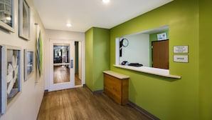 Un pasillo con pared verde, suelo de madera, un mostrador de recepción, un reloj y una puerta que da a otra habitación.