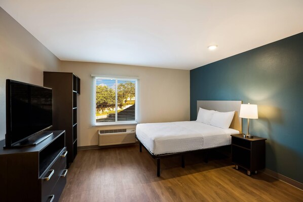 Habitación de hotel con cama, televisión, mesita de noche con lámpara y ventana con persianas.
