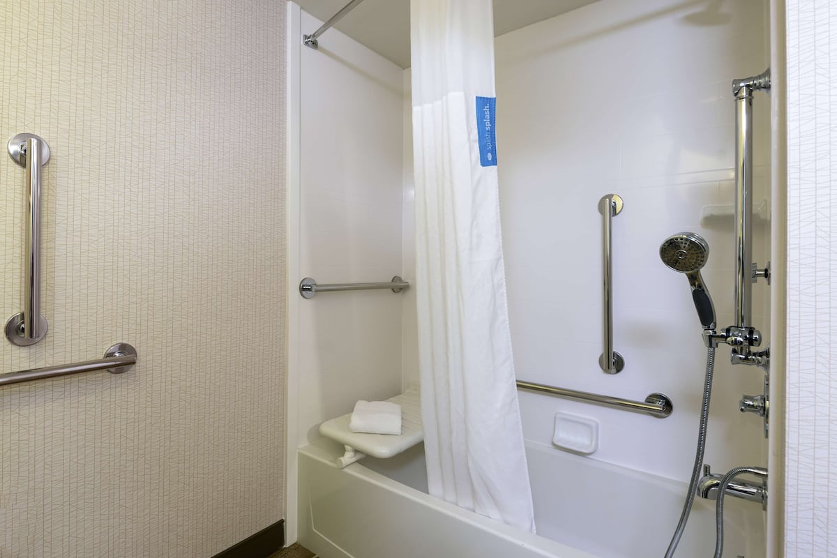 A bathroom with a shower, grab bars, a toilet, and a towel rack.