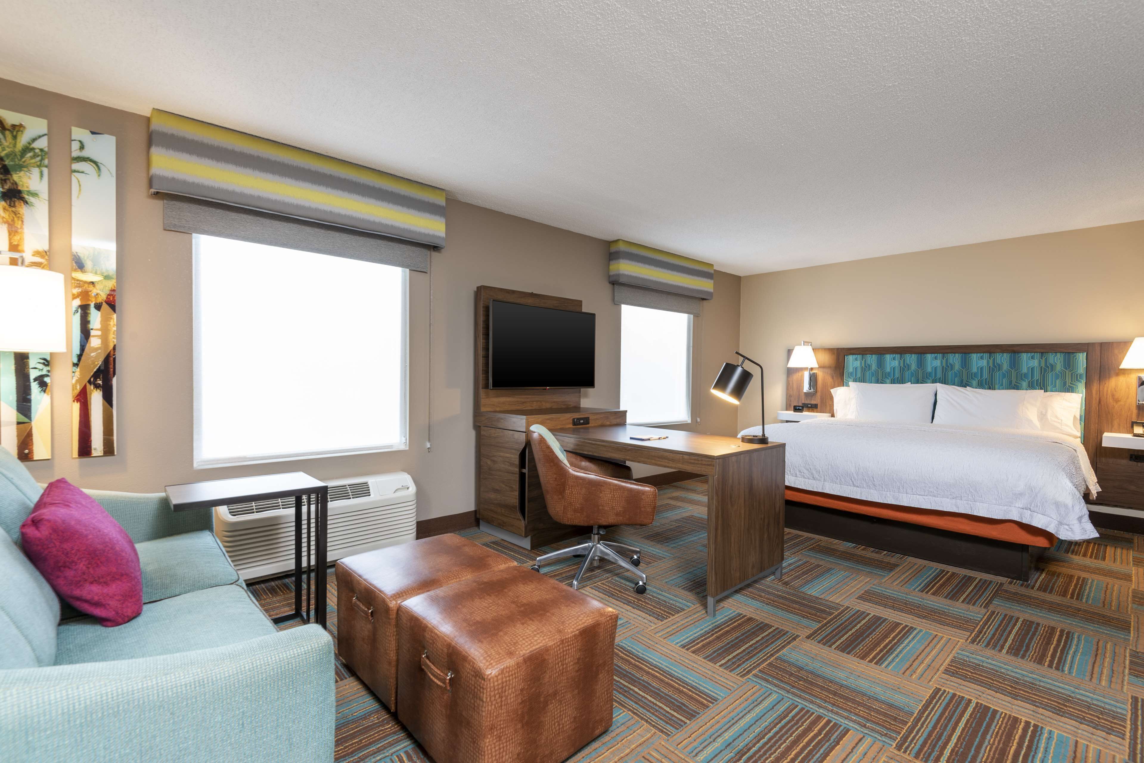 A hotel room with a bed, a desk, a chair, a television, and a large window.