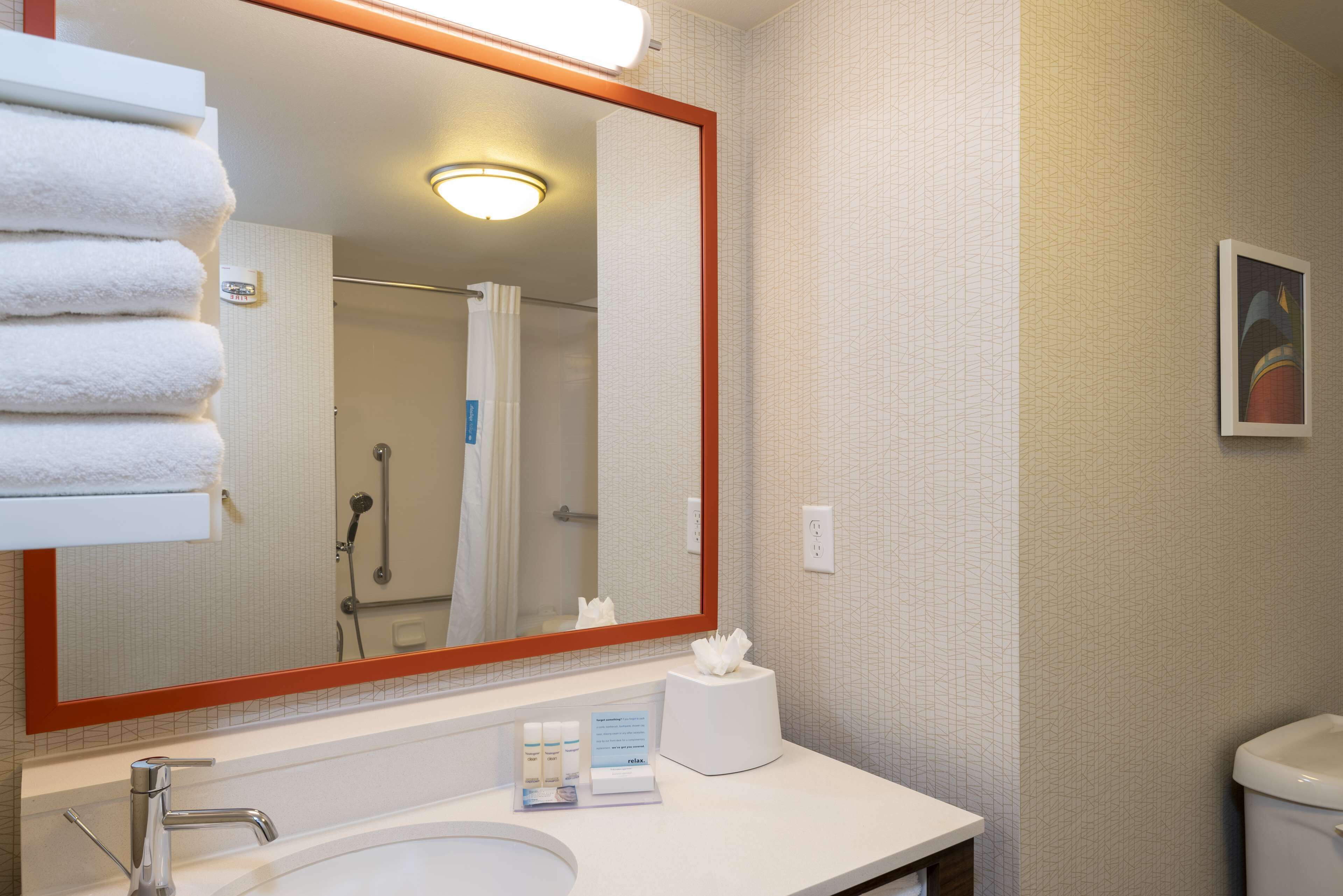A bathroom with a large mirror, a sink, a towel rack, a toilet, and a framed picture on the wall.