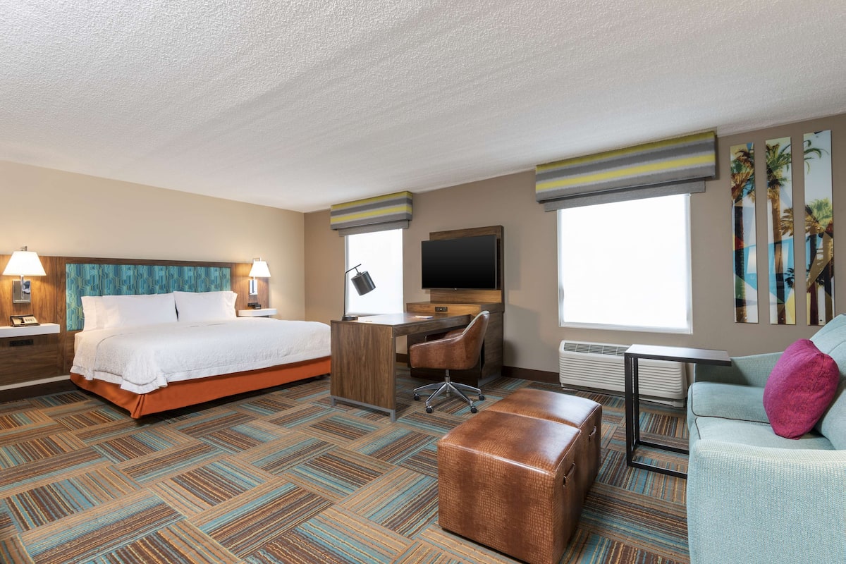 A hotel room with a large bed, a desk, a chair, a small table, a sofa, and a TV.