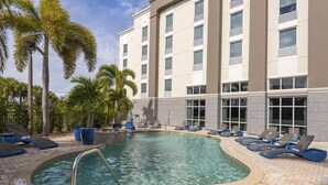 A swimming pool with lounge chairs and palm trees, surrounded by a building with multiple windows. - Hampton Inn & Suites Fort Myers - Colonial Blvd (Fort Myers)