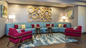 A modern living room with a blue sofa, red armchairs, and a coffee table. There are two lamps and a wall art piece above the sofa. - Hampton Inn & Suites Fort Myers - Colonial Blvd (Fort Myers)
