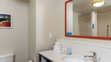 Une salle de bain avec un lavabo blanc, un miroir avec un cadre rouge, des toilettes et un distributeur de serviettes.