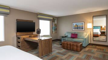A hotel room with a bed, a desk with a flat-screen TV, a sofa, a small table, a suitcase, and a painting on the wall.