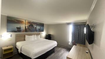 Hotelkamer met een groot bed, een houten nachtkastje, een bureau met stoel, een flatscreen televisie aan de muur en een schilderij van een pier en zonsondergang.