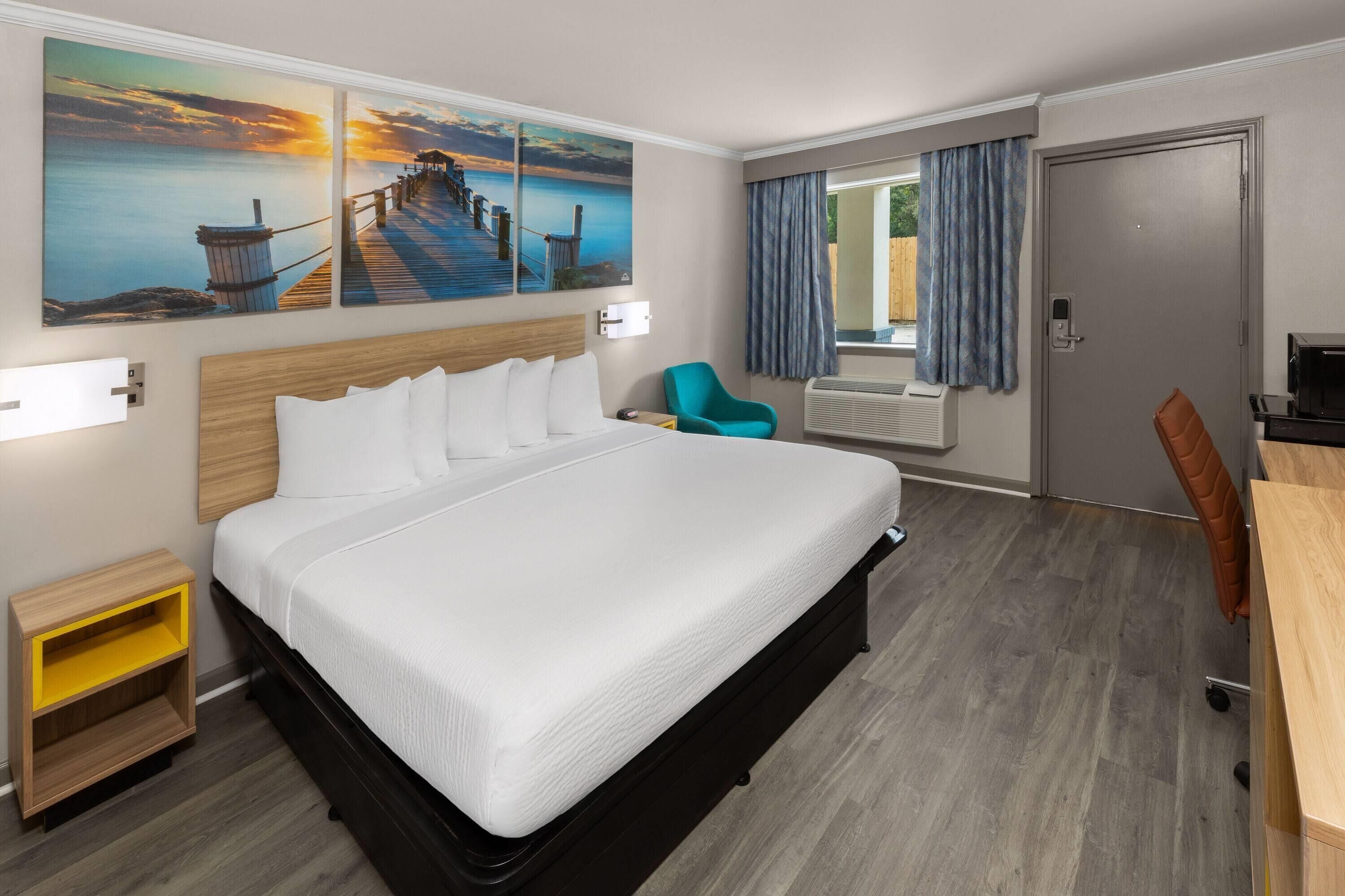 Ein Hotelzimmer mit einem großen Bett, einem Schreibtisch, einem Stuhl und einem Fenster mit Vorhängen.
