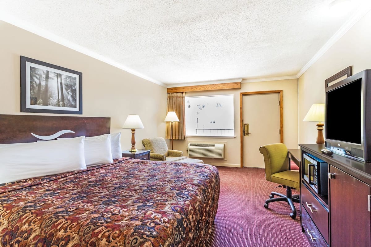 A hotel room with a large bed, a television, a desk with a computer, a chair, and a window with curtains.