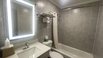 Une salle de bain avec un grand miroir, un lavabo, des toilettes et une baignoire.
