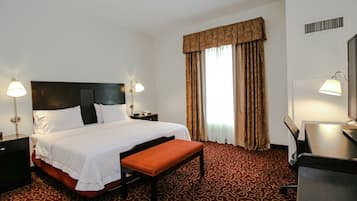 Une chambre d’hôtel avec un grand lit, deux tables de chevet, un bureau avec une chaise et une fenêtre avec des rideaux.