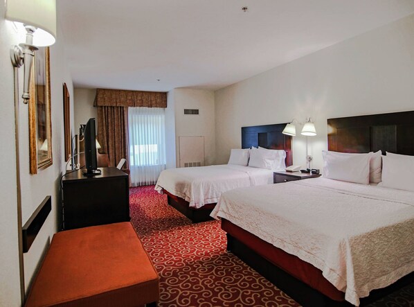 A hotel room with two beds, a desk, a chair, a TV, and a window with curtains.