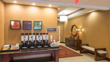 A hotel reception area with a coffee station, an elevator sign, and a bench.