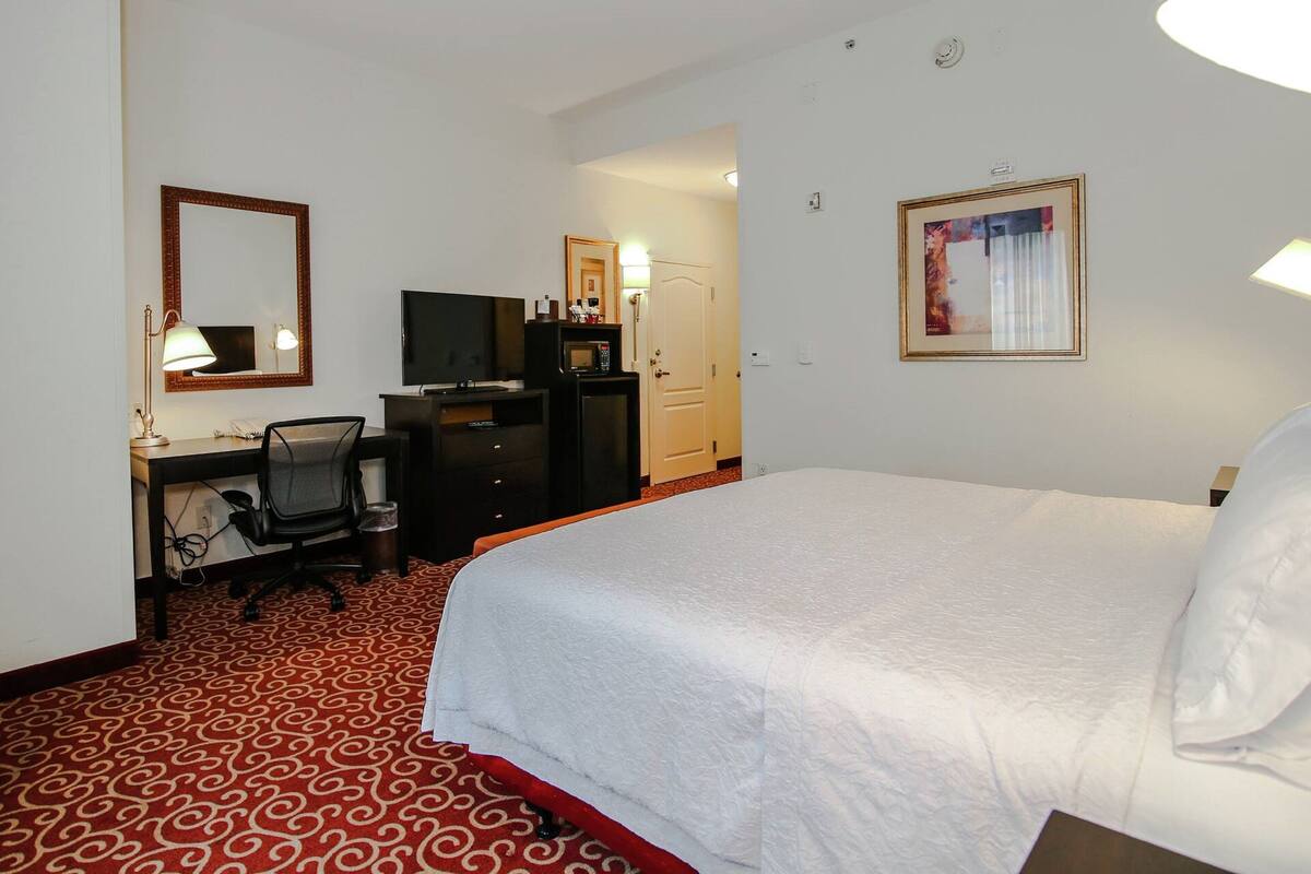 A hotel room with a bed, a desk with a chair, a television, a microwave, and a wardrobe.