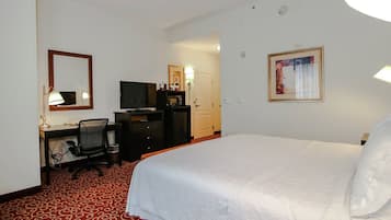 A hotel room with a bed, a desk with a chair, a television, a microwave, and a wardrobe.