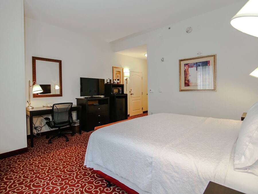 A hotel room with a bed, a desk with a chair, a television, a microwave, and a wardrobe.