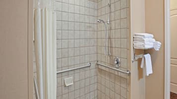 Ducha en esquina con azulejos color beige, barra de apoyo y toallero con toallas dobladas.