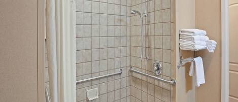 Ducha en esquina con azulejos color beige, barra de apoyo y toallero con toallas dobladas.