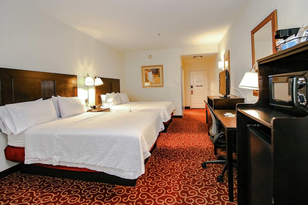 A hotel room with two beds, a desk, a TV, and a microwave.