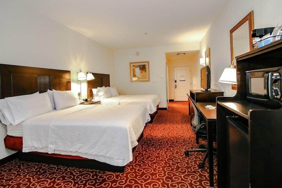 A hotel room with two beds, a desk with a computer, a TV, and a microwave.
