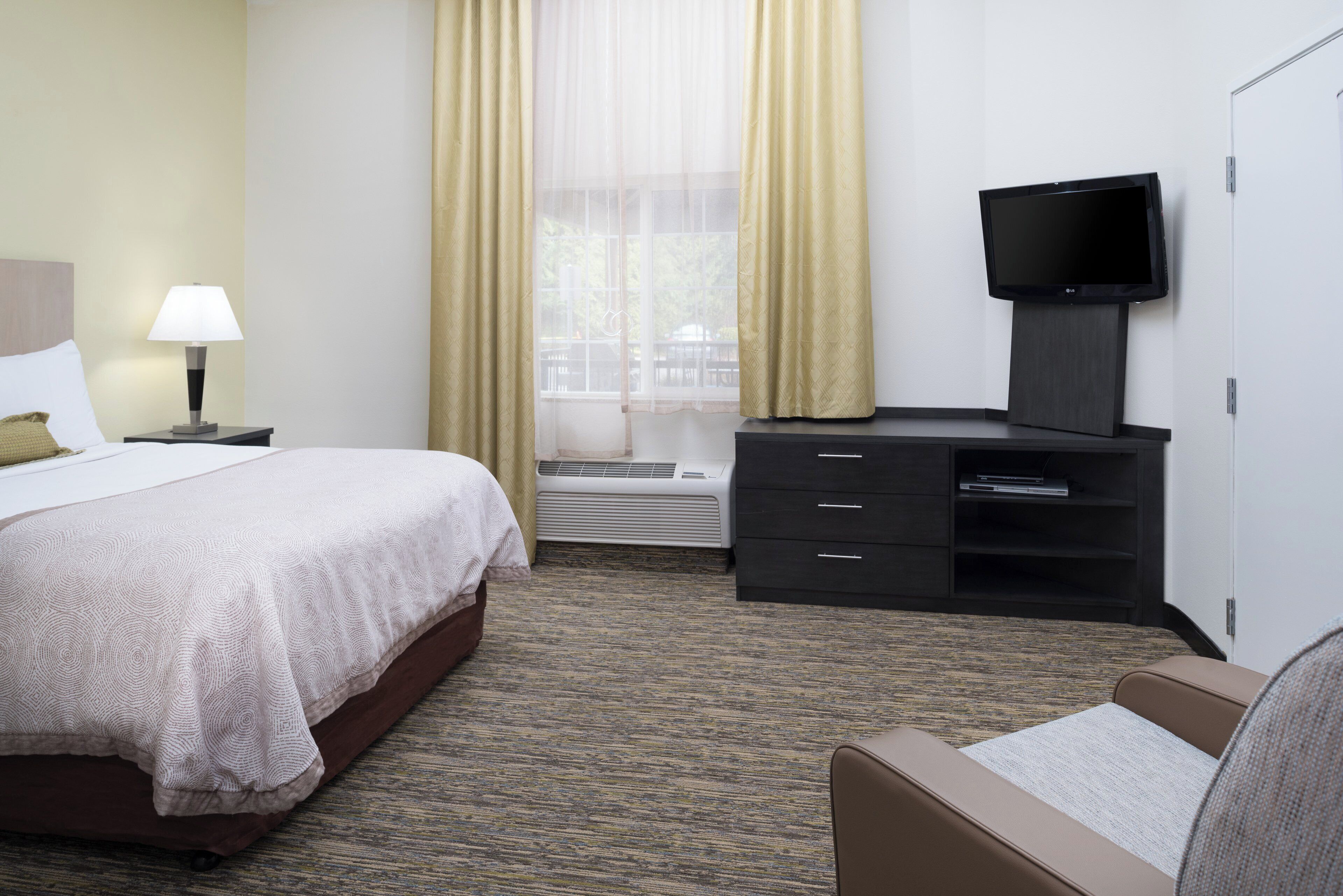 Habitación de hotel con cama, escritorio con televisor de pantalla plana, silla y ventana con cortinas.