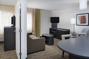Una habitación de hotel con televisión de pantalla plana, un sofá, una mesa de comedor y una silla.