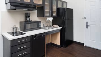 Une cuisine moderne avec des meubles de couleur noire, un four à micro-ondes encastré, une machine à café, un évier et un réfrigérateur noir.