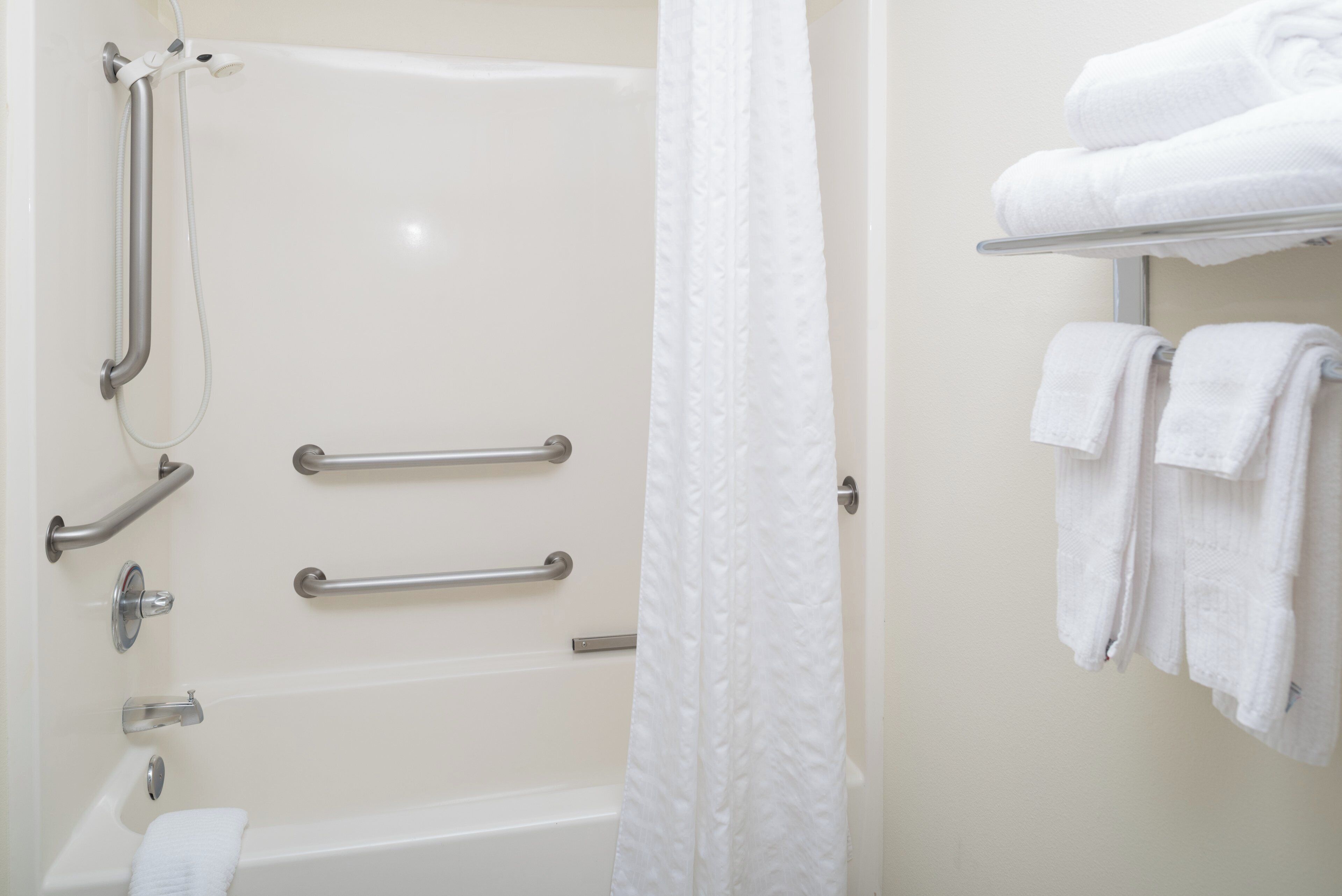 A bathroom with a bathtub, a shower with grab bars, and a towel rack with towels.