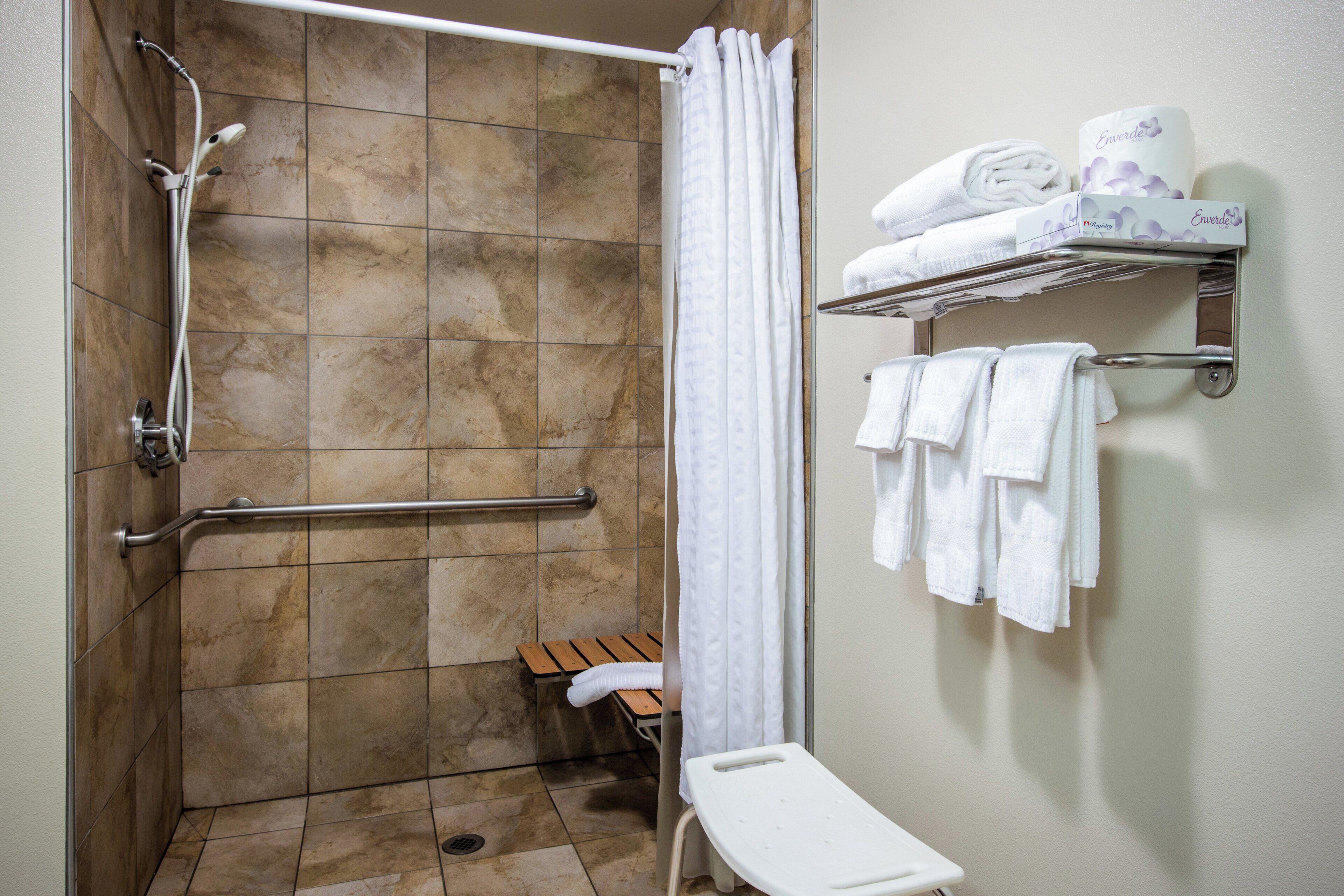 A shower area with a handrail, a bench, and a shelf with towels.