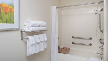 A bathroom with a bathtub, a shower, and a handrail. There are towels on a rack and a picture on the wall.
