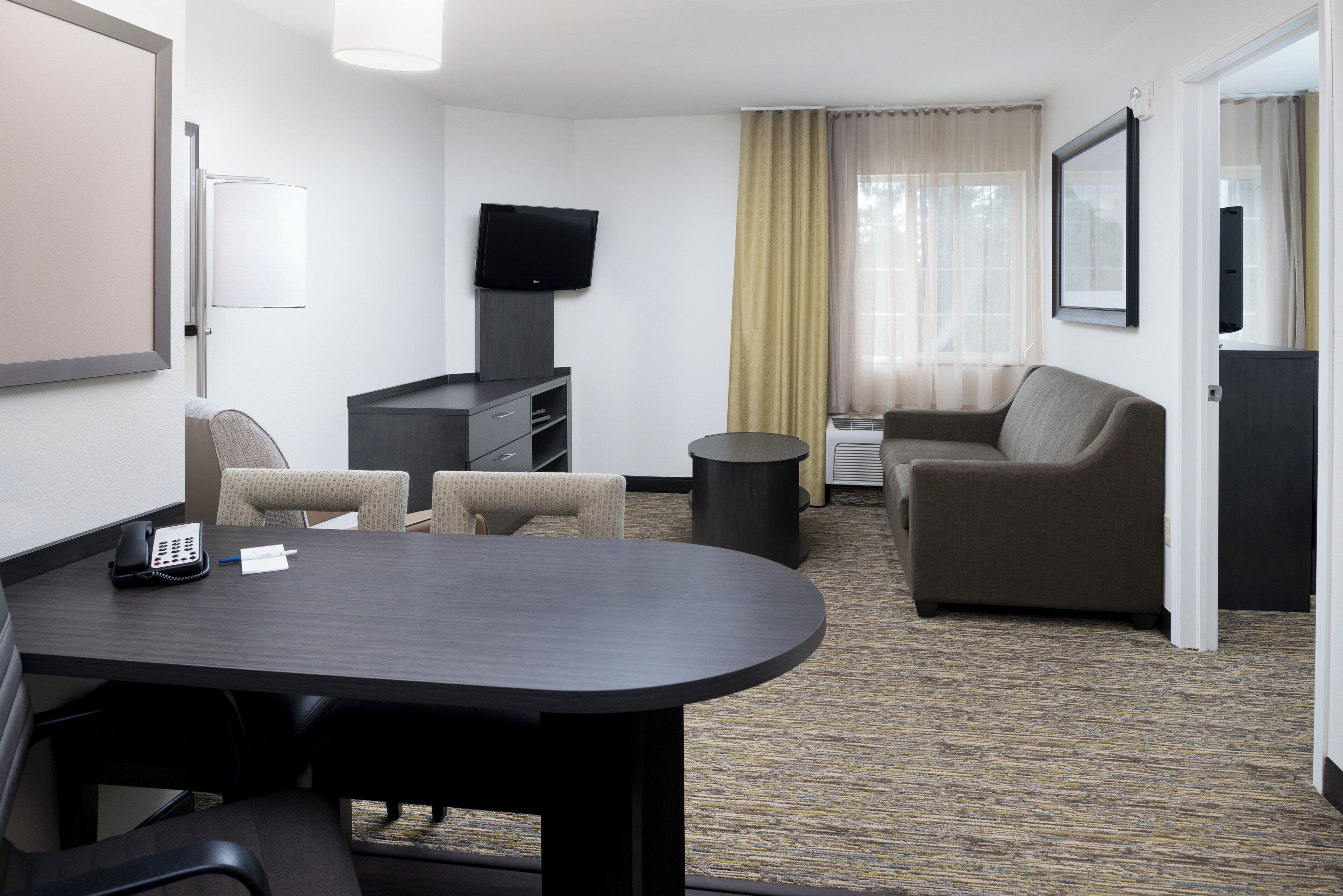 A hotel room with a desk, two chairs, a sofa, a television, and a window with curtains.