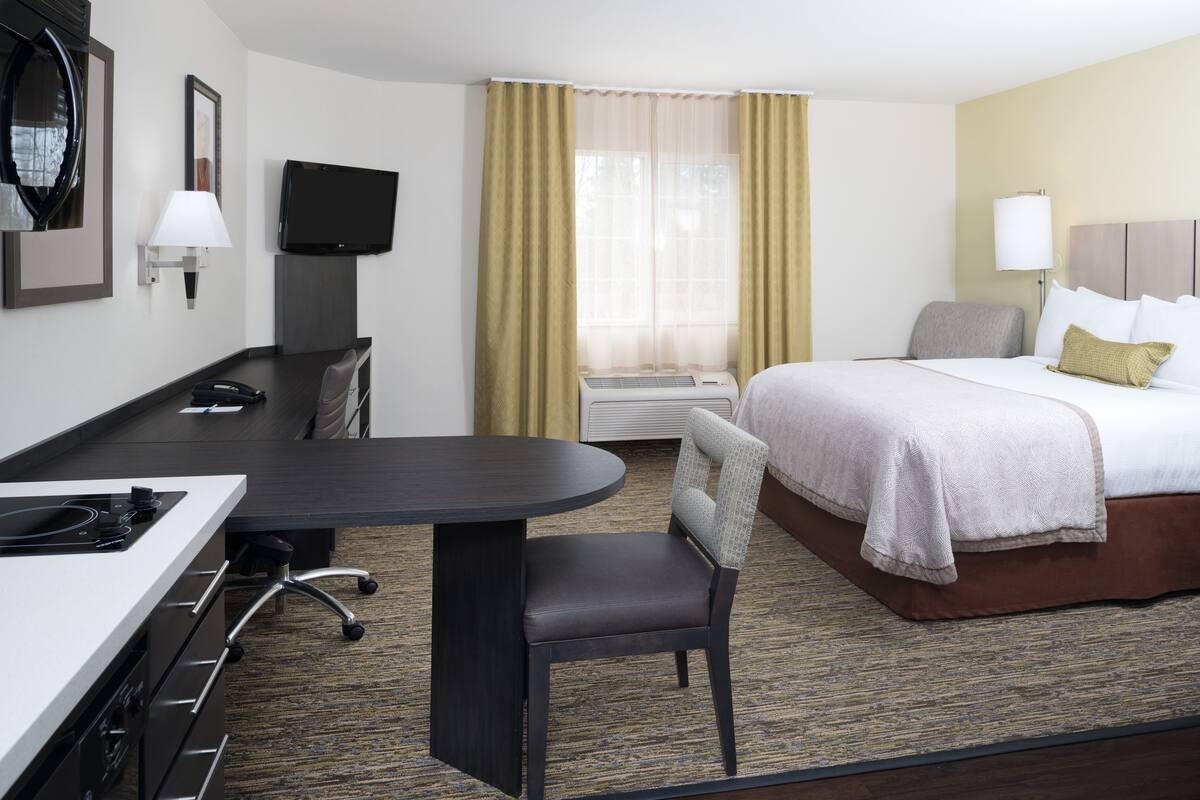 Ein Hotelzimmer mit Bett, Schreibtisch, Stuhl, Fernseher und einem Fenster mit Vorhängen.