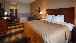 Une chambre d’hôtel avec un grand lit, un bureau, une chaise, une petite table, une lampe et un tableau au mur.