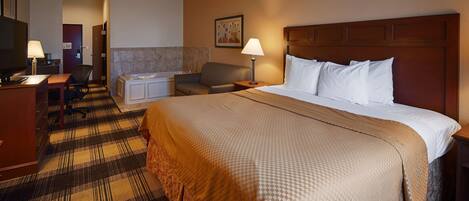 A hotel room with a large bed, a desk, a chair, a small table, a lamp, and a painting on the wall.