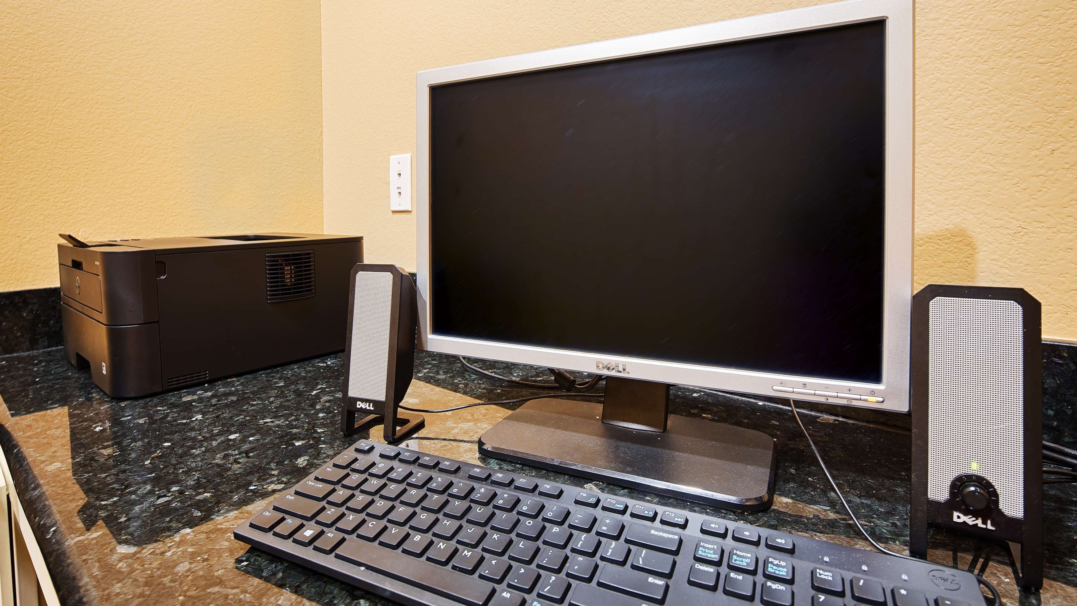 Uma configuração de computador com monitor, teclado e colunas sobre um balcão de granito.