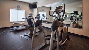 Une salle de sport équipée de tapis de course, de vélos elliptiques et d’un mur recouvert de miroirs.