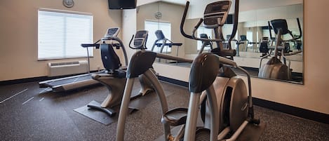 A gym with treadmills, elliptical machines, and a mirrored wall.