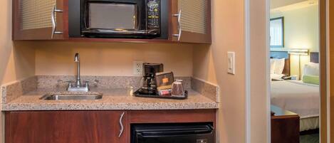 A compact hotel kitchenette with a microwave, sink, and a small refrigerator.