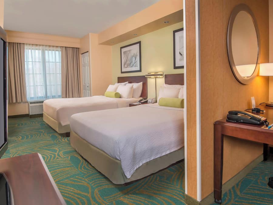 A hotel room with two beds, a desk with a telephone, and a television.