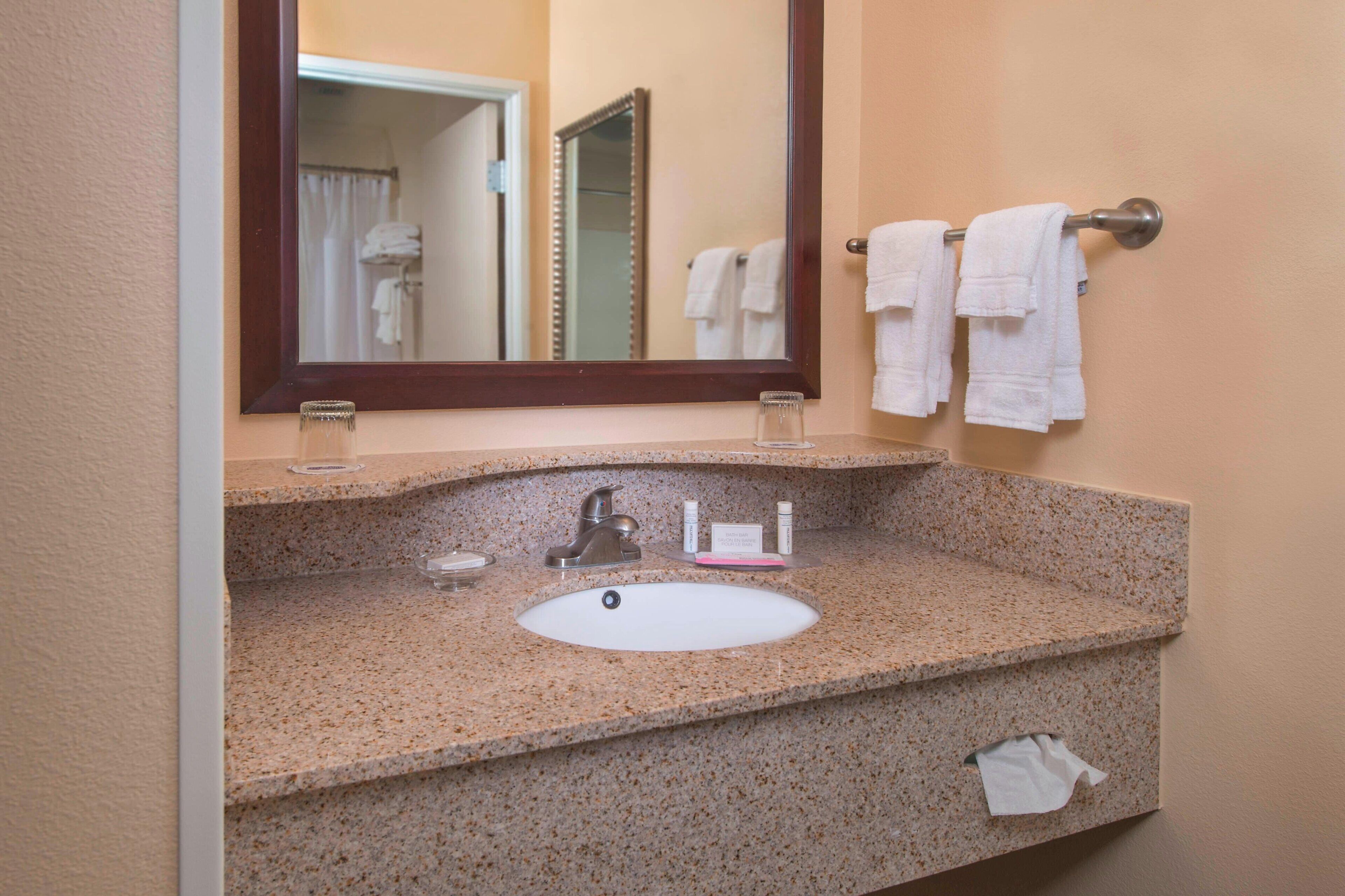 A bathroom with a granite countertop, a sink, a mirror, and a towel rack with towels.