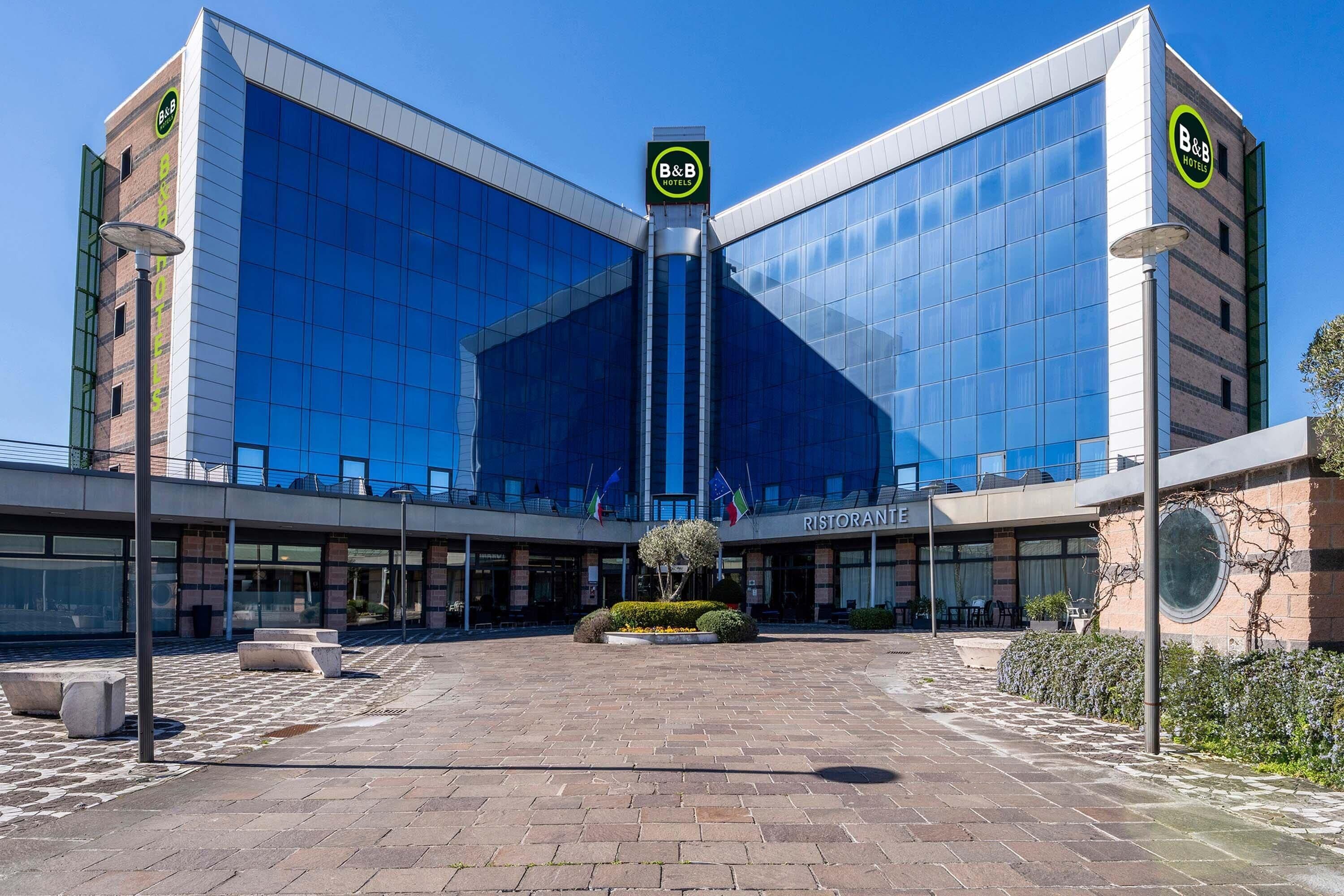 A modern hotel with a glass facade, a central courtyard, and a restaurant named 'Ristorante' on the ground floor.