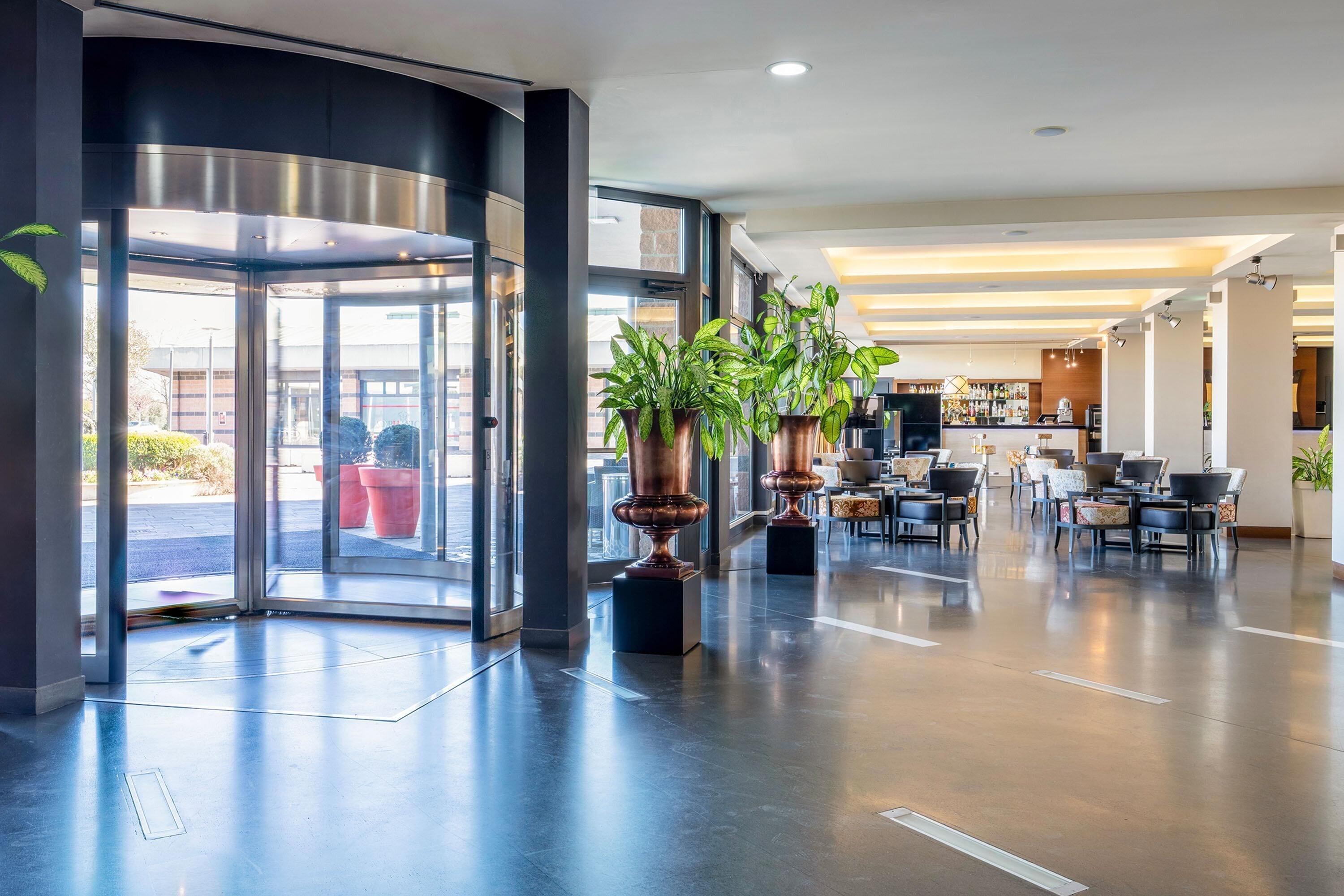 Eine moderne Lobby mit einer Glastür, Pflanzen in Töpfen, einer Sitzecke und einer Bar.