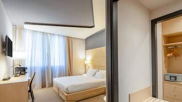 Habitación de hotel con cama, escritorio con lámpara, televisor y armario.