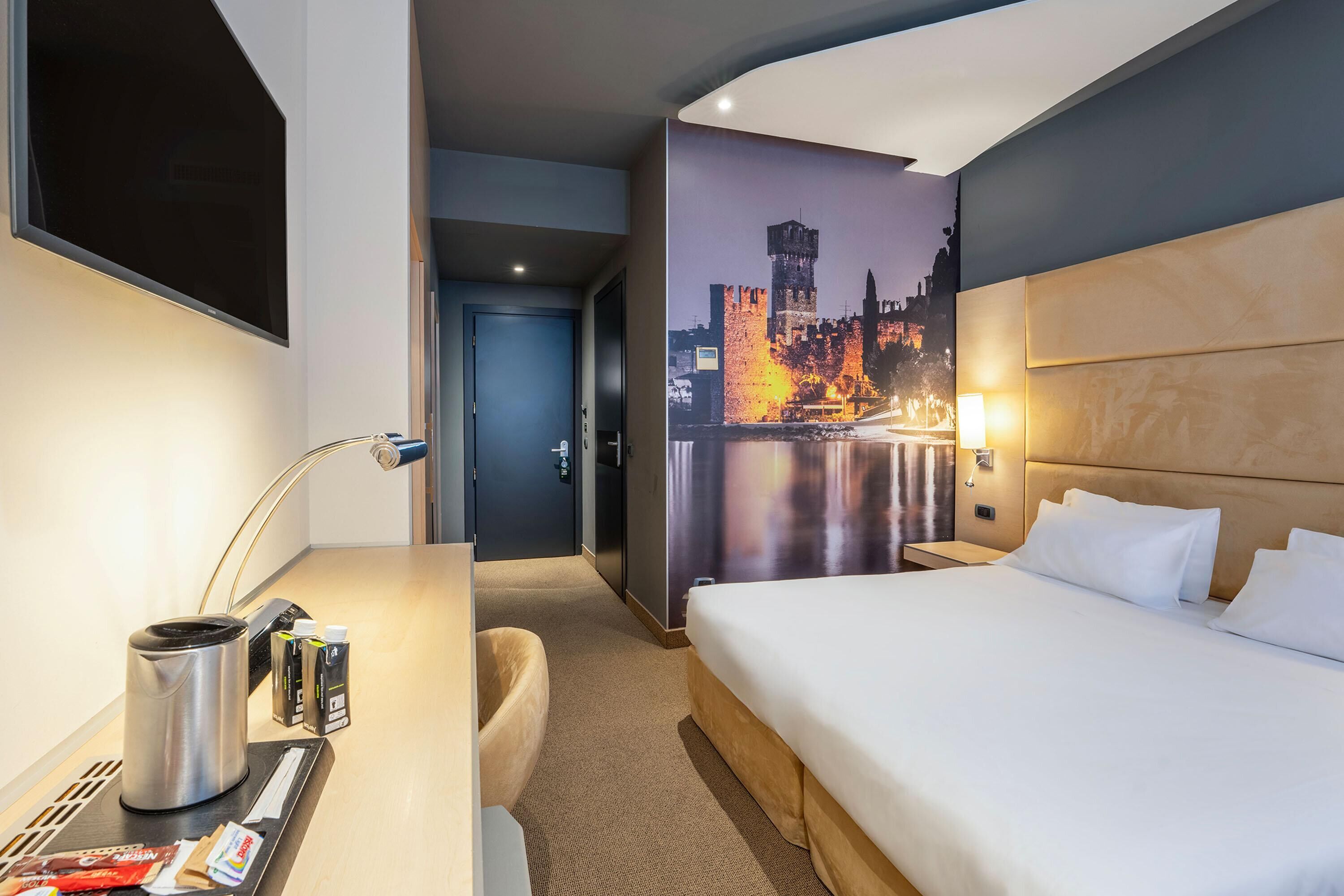 Een hotelkamer met een bed, bureau en een stadsgezichtmuurschildering.