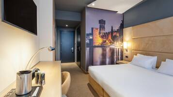 Een hotelkamer met een bed, bureau en een stadsgezichtmuurschildering.